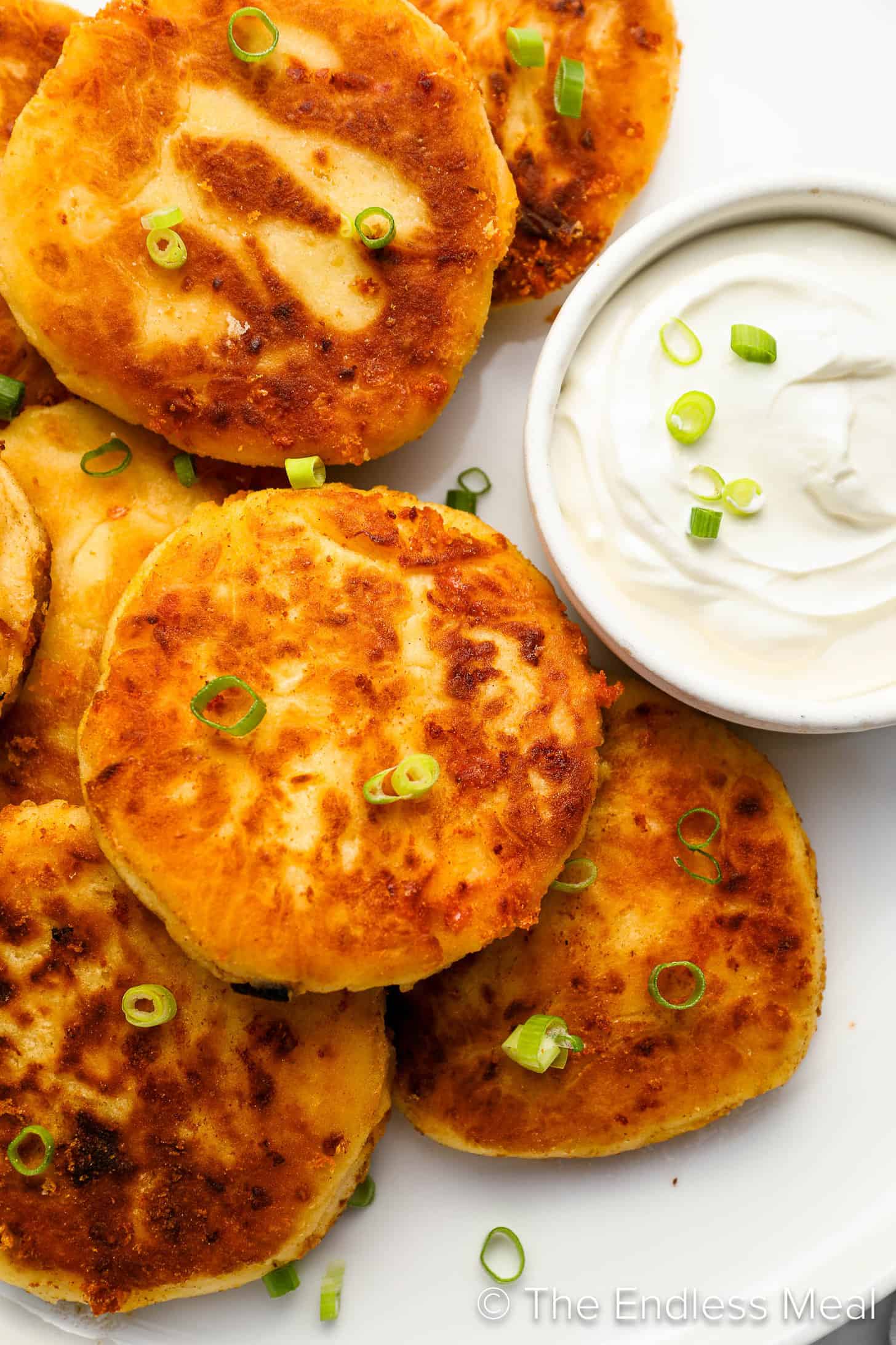 A close up of Mashed Potato Cakes with sour cream on a serving plate.