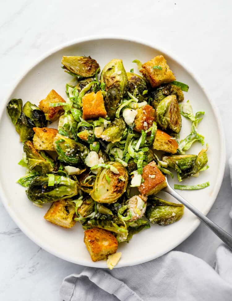 Brussels Sprouts Caesar Salad on a white plate with a fork
