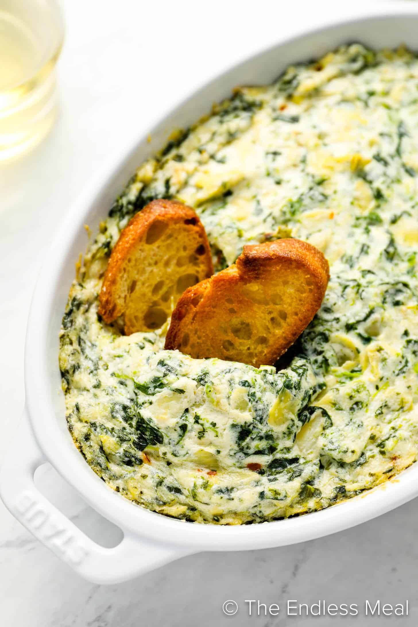 Two pieces of bread dipping into Hot Spinach Artichoke Dip