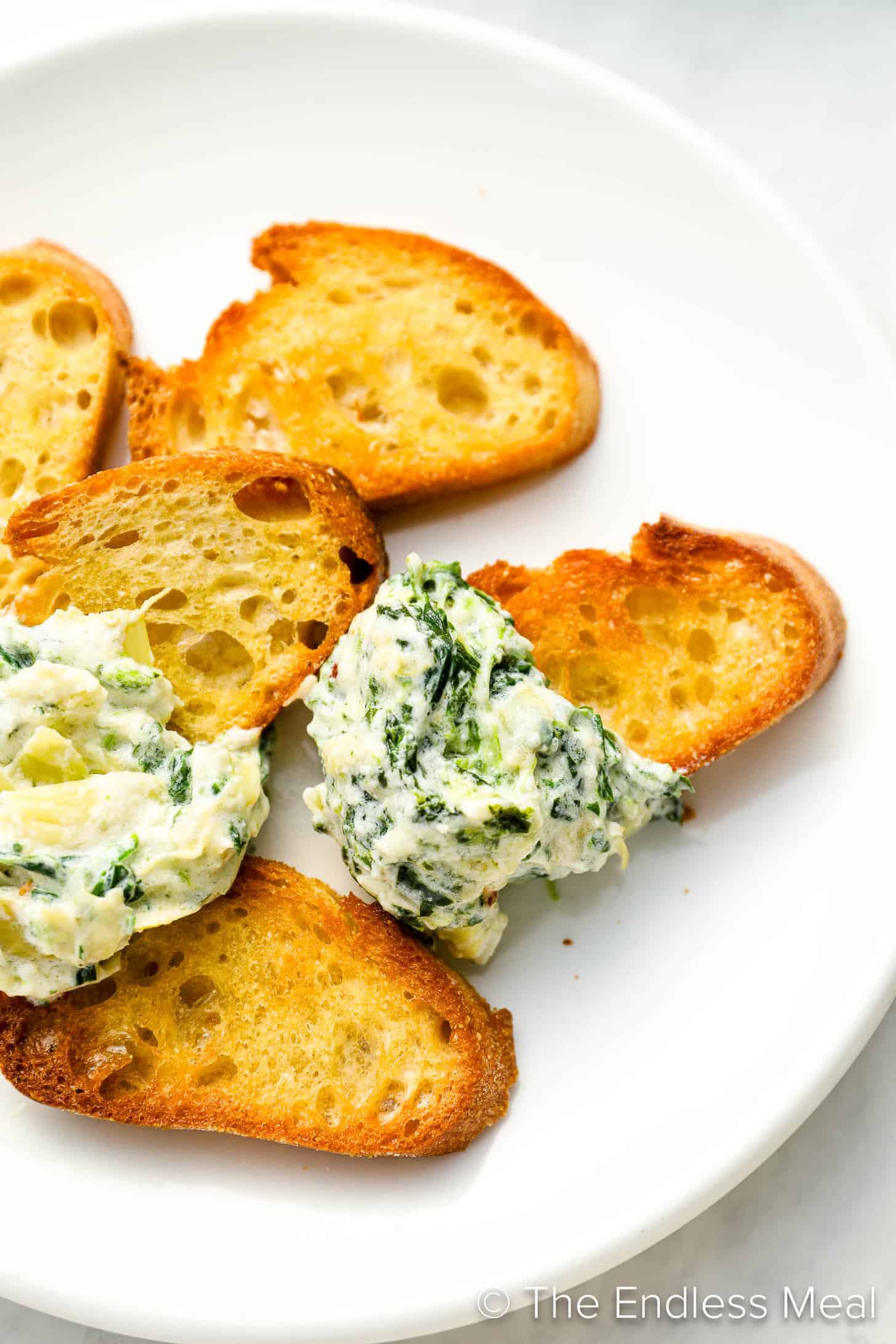 An appetizer plate with crostini and Hot Spinach Artichoke Dip