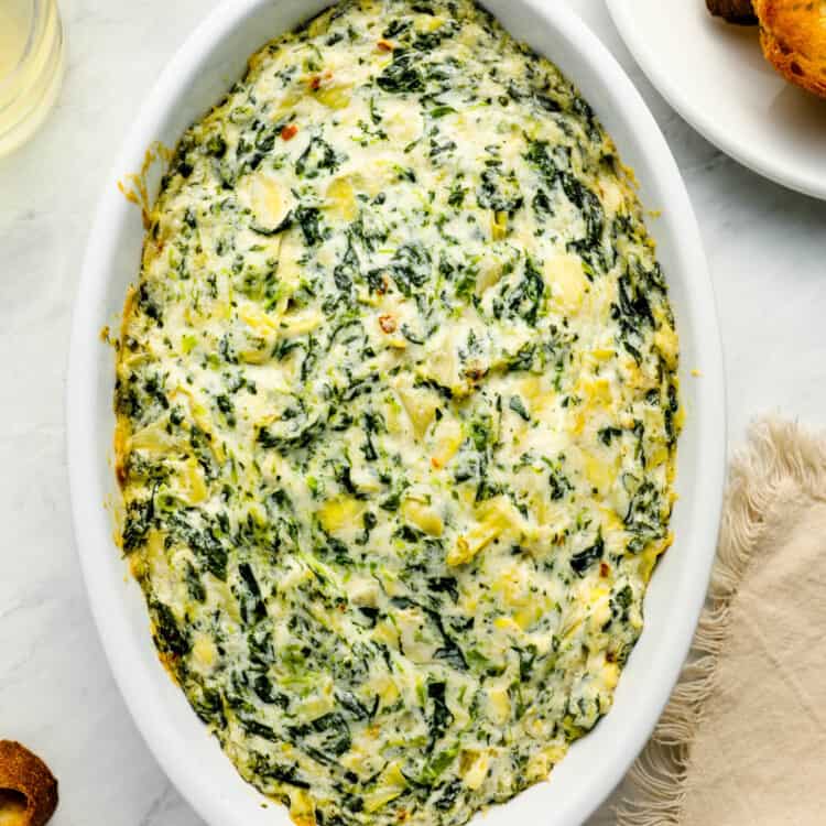 A baking dish of Hot Spinach Artichoke Dip on an appetizer table.