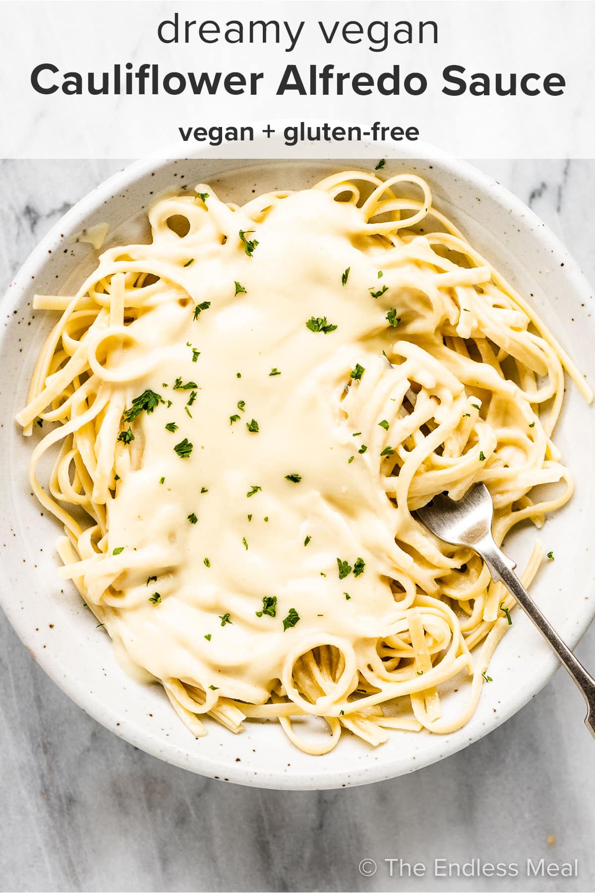 A white plate with vegan fettuccini alfredo and a fork and the recipe title on top of the picture.