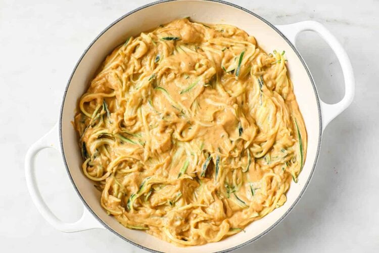 Large white pan filled with creamy dairy-free pumpkin alfredo pasta, mixed with zucchini noodles in a thick, orange-colored sauce.