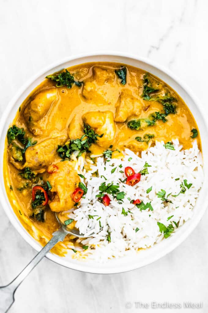A bowl of rice and Thai chicken curry with a spoon inside.