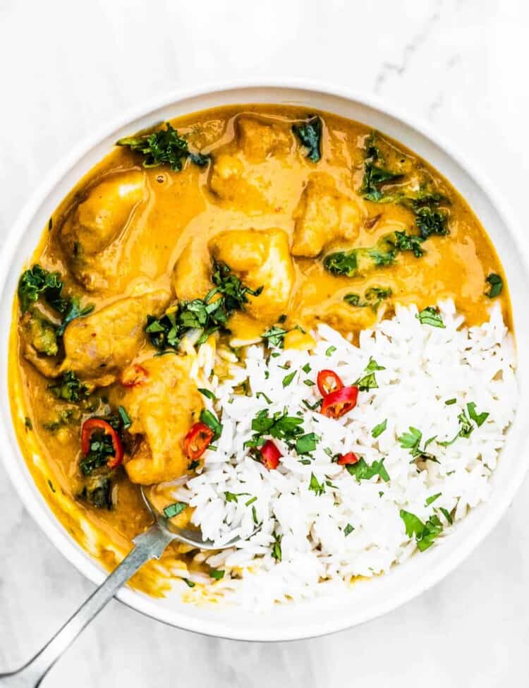 A bowl of rice and Thai chicken curry with a spoon inside.