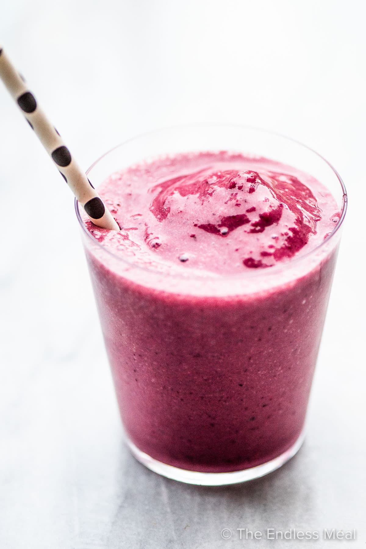 Pink chia berry smoothie in a glass with a black and white straw.