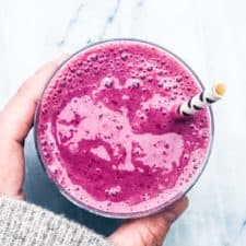 A hand holding a glass of chia berry smoothie
