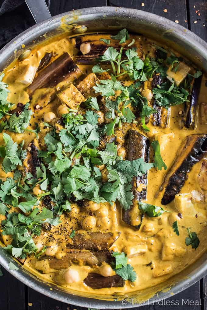 A close up of a yellow-colored eggplant curry in a pot with cilantro on the top.