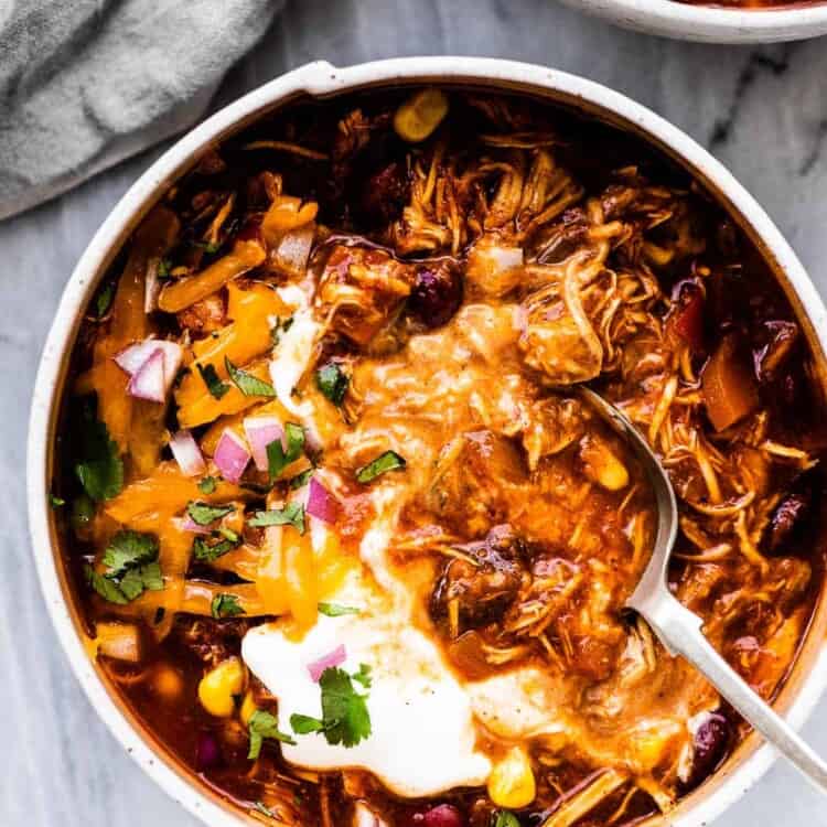 A spoon in a white bowl filled with crockpot chicken chili.