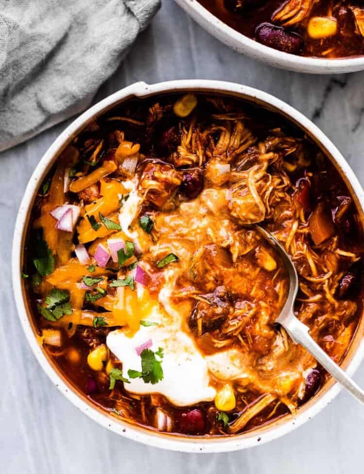 A spoon in a white bowl filled with crockpot chicken chili.