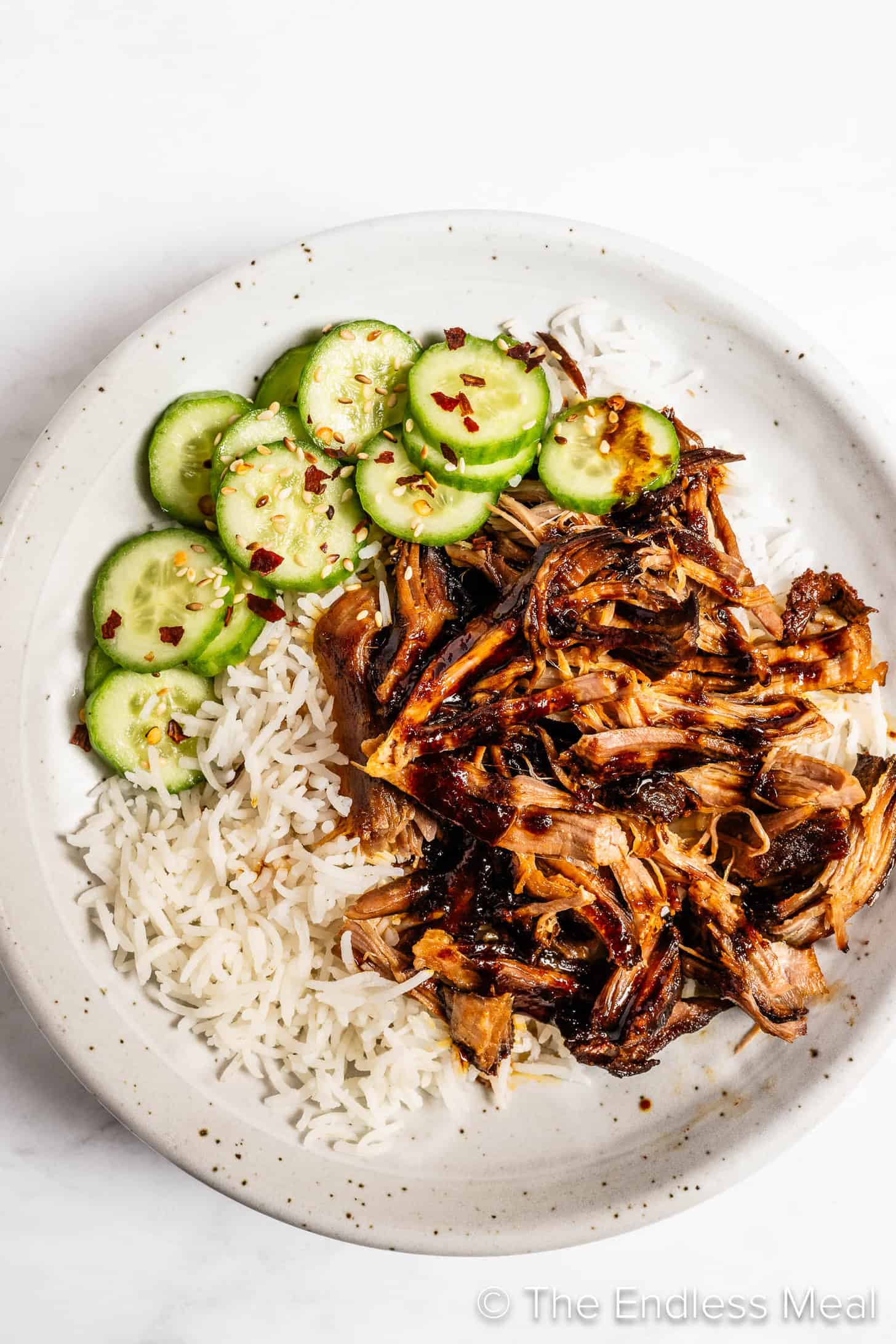 Korean Pulled Pork on a dinner plate with rice and cucumbers