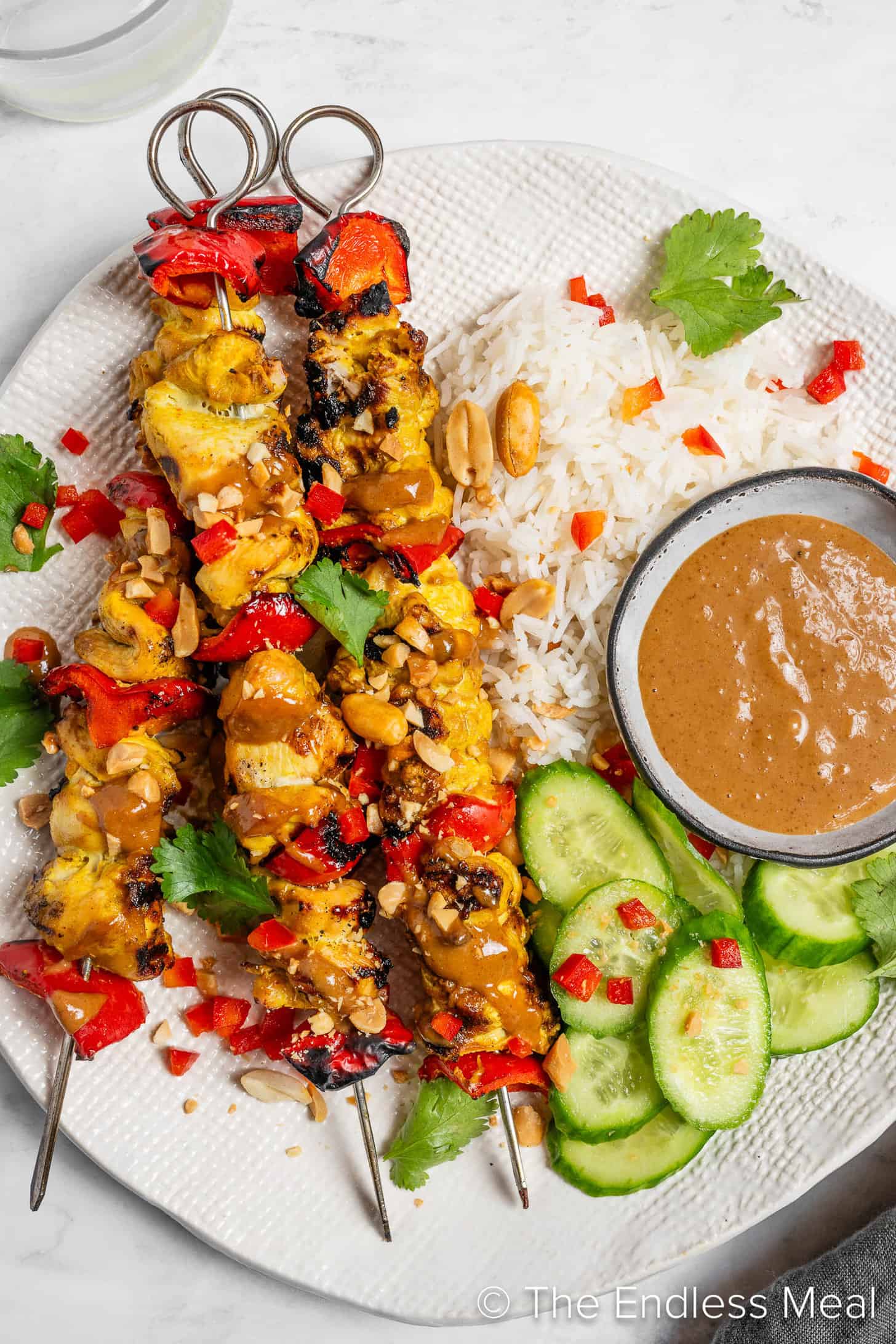 Chicken Satay Skewers on a dinner plate with rice and cucumbers