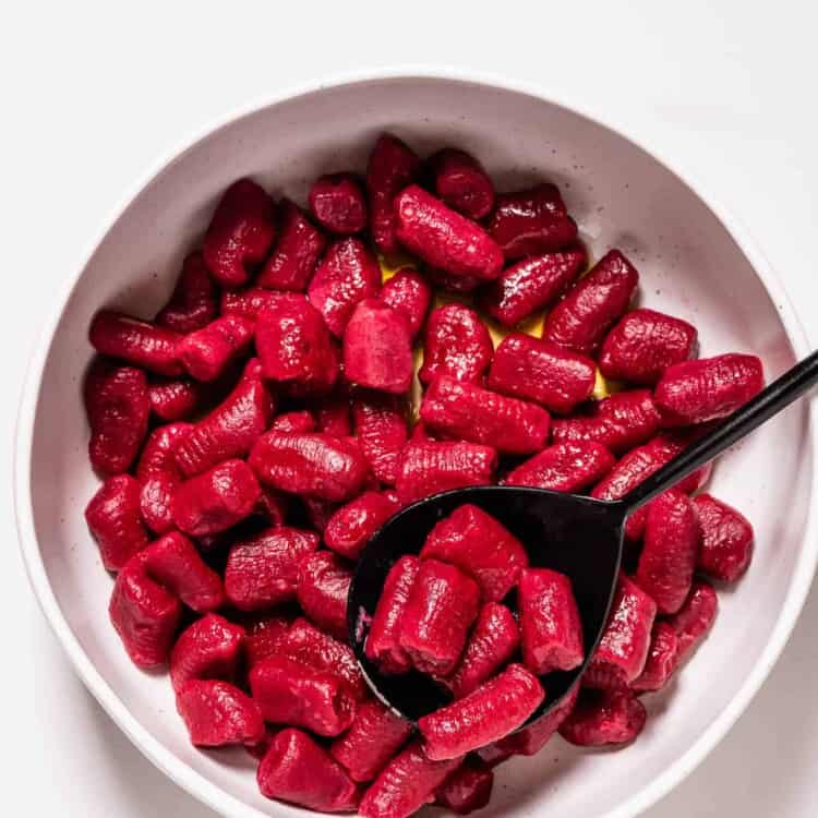 beet gnocchi in a white dish with a serving spoon