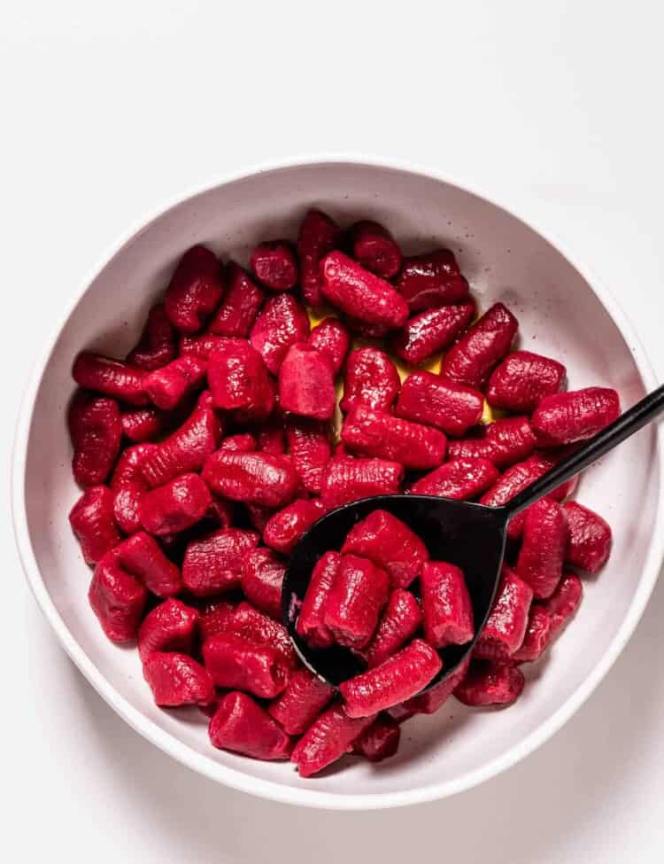 beet gnocchi in a white dish with a serving spoon