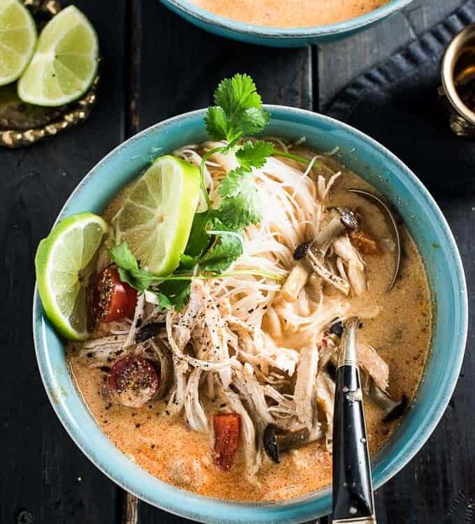 A blue bowl filled with crockpot Thai chicken soup with a spoon it it on a black wooden table.