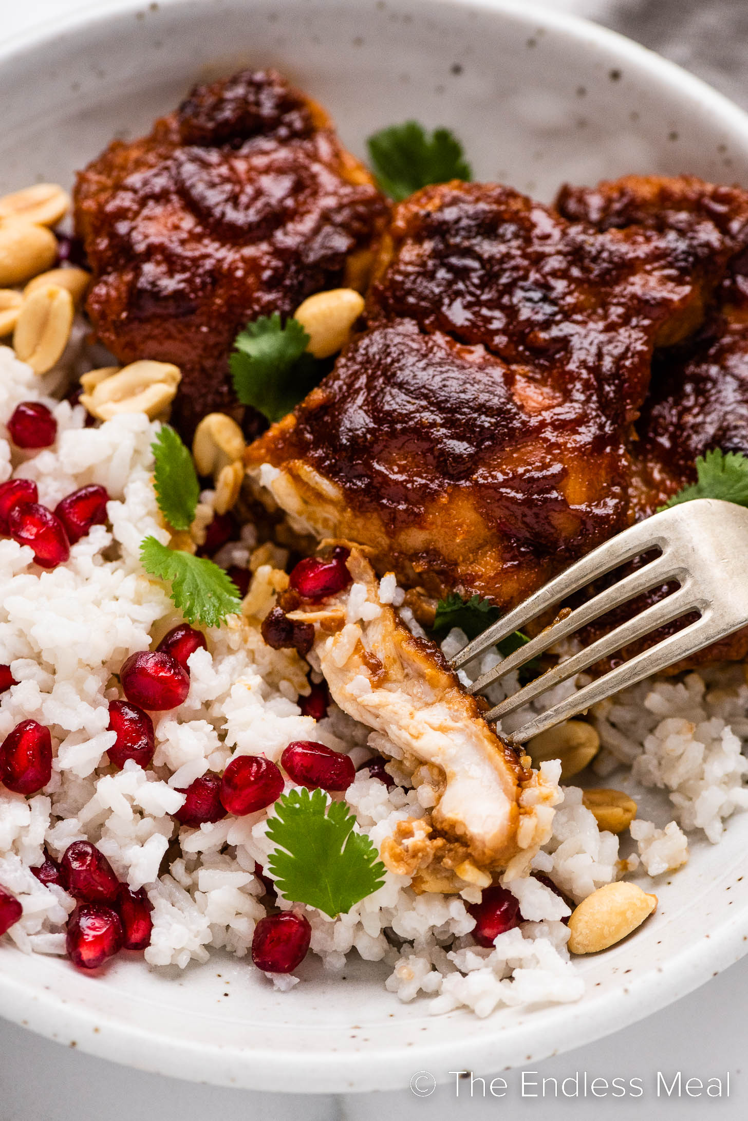 a close up of a fork with a piece of Pomegranate Chicken.