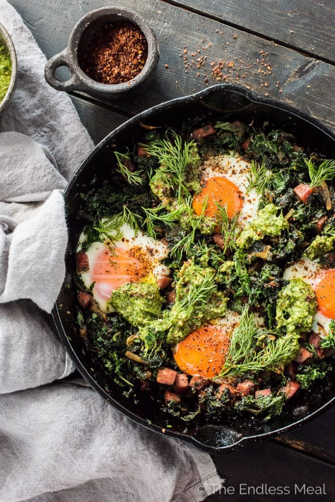 This easy to make green shakshuka is a playful take on a Green Eggs and Ham Recipe. The eggs are nestled into caramelized onions, farmer's sausage, and kale and topped with a delicious lemony dill pesto. This healthy breakfast recipe is bursting with flavor and naturally paleo + Whole30 approved. | theendlessmeal.com