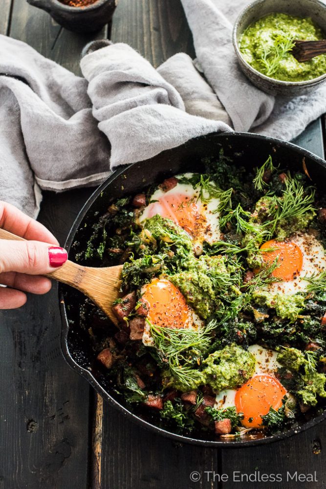 This easy to make green shakshuka is a playful take on a Green Eggs and Ham Recipe. The eggs are nestled into caramelized onions, farmer's sausage, and kale and topped with a delicious lemony dill pesto. This healthy breakfast recipe is bursting with flavor and naturally paleo + Whole30 approved. | theendlessmeal.com