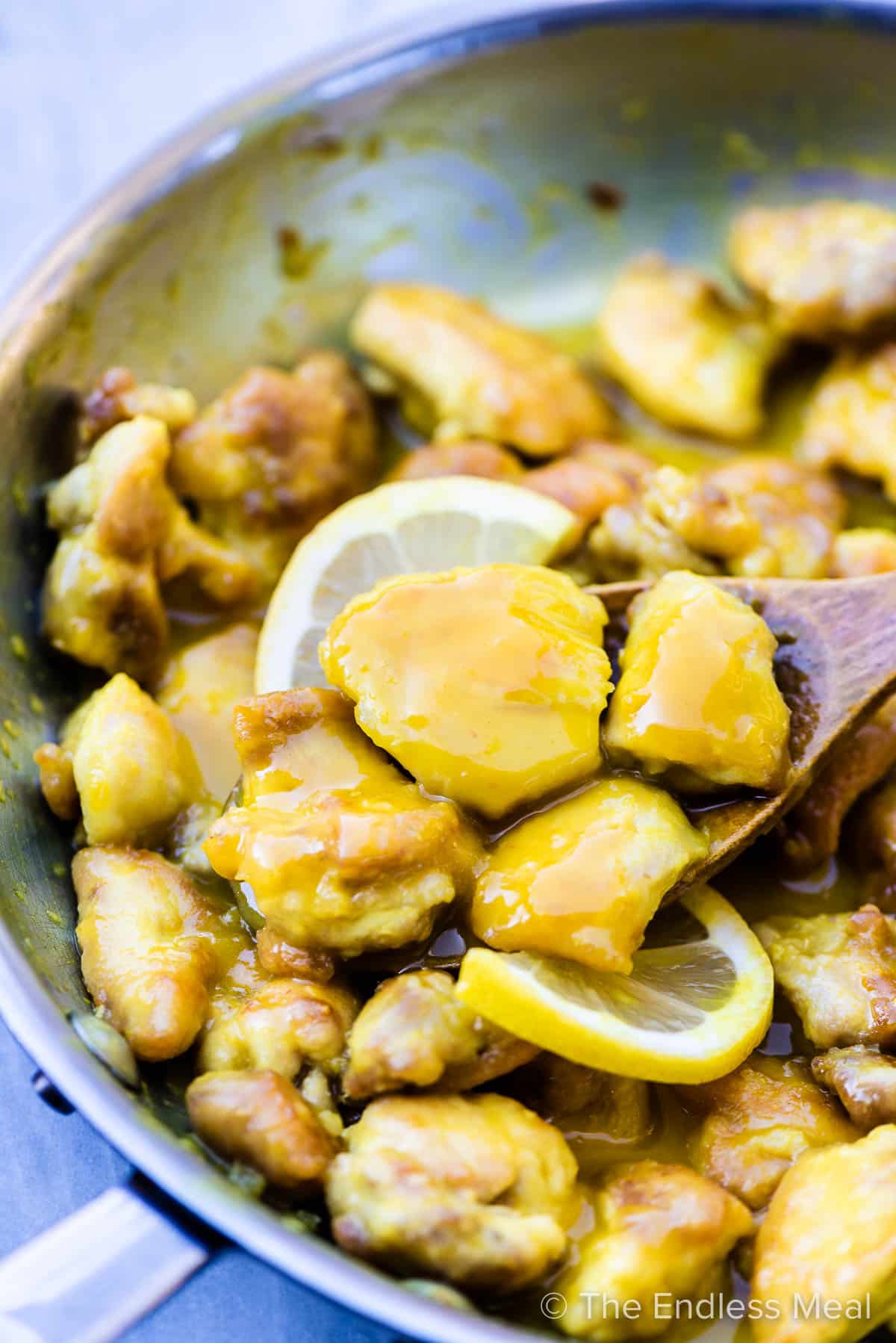 Tender chunks of lemon chicken with lots of sauce in a pan.