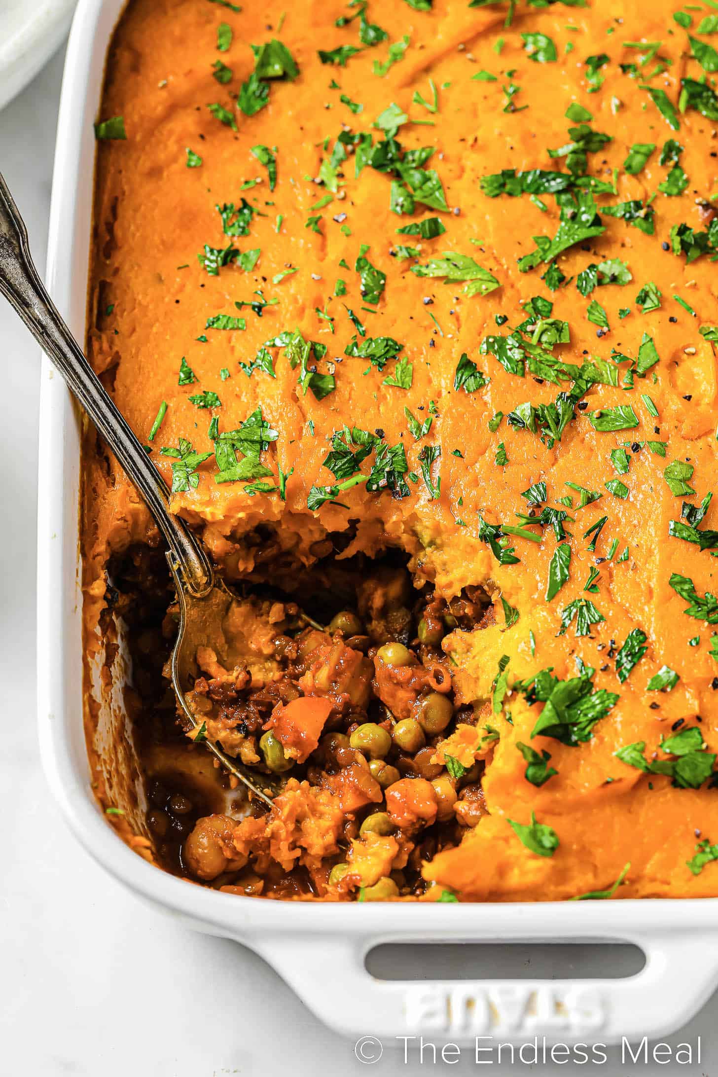 a spoon scooping some curried Vegan Shepherd's Pie from a casserole dish