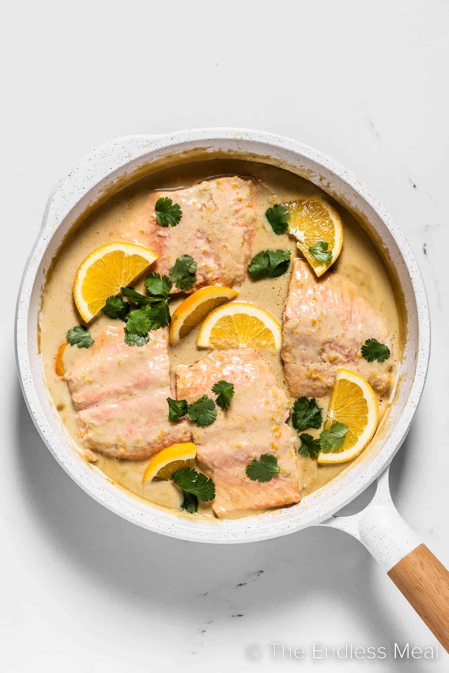 Looking down on Coconut Orange Poached Salmon in a white frying pan.