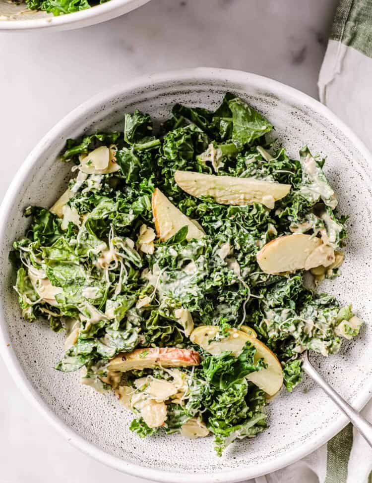 Creamy Kale tahini Salad in a white bowl with a fork.