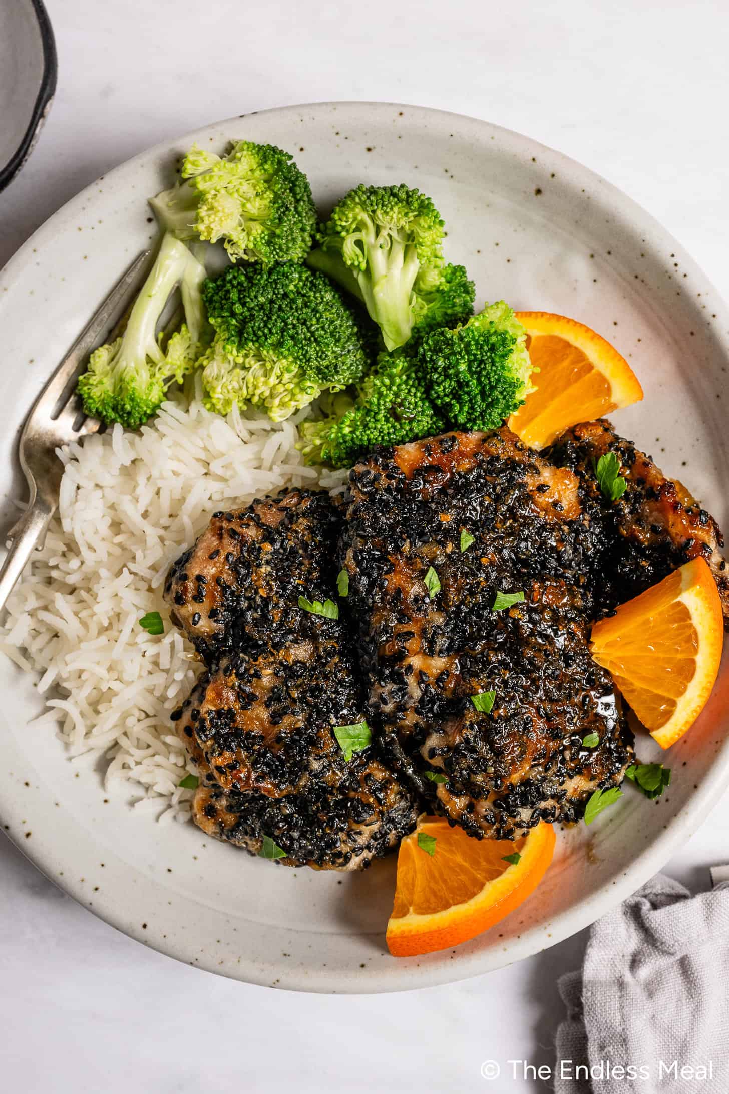 Sesame orange chicken on a dinner plate with rice and broccoli