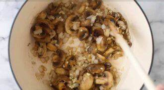 Chopped mushrooms, onions, and garlic being sautéed in a light-colored pot for turkey mushroom soup, stirred with a wooden utensil.