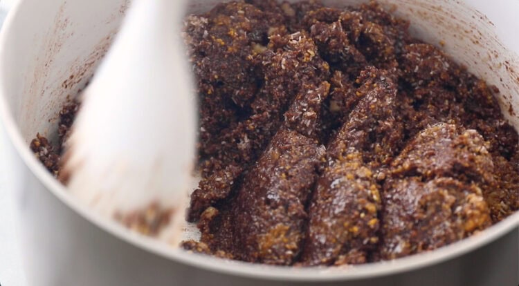 Close-up of a pot containing a thick, brown mixture being stirred with a white utensil.