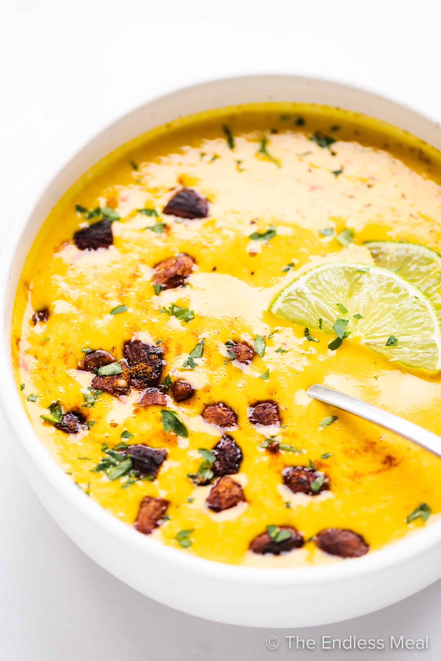 Sweet Potato Turmeric Soup in a white bowl with a spoon.