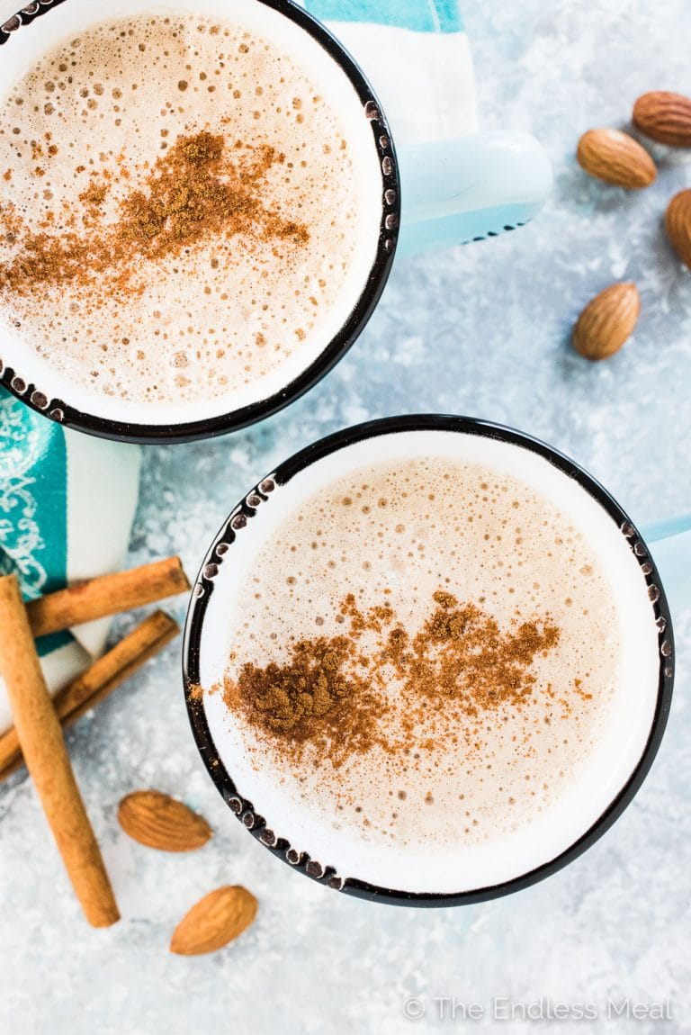 2 almond butter lattes in blue mugs with cinnamon sprinkled on top.