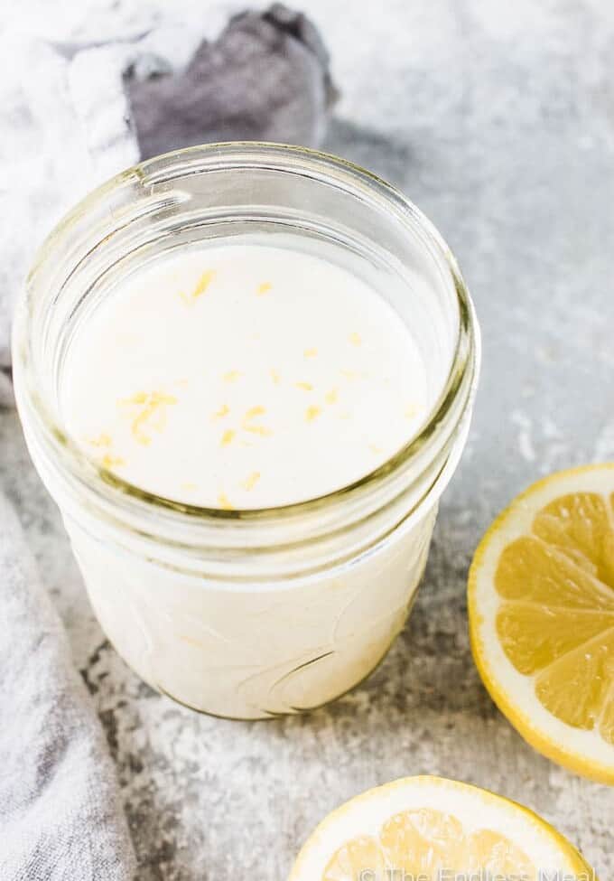Lemon buttermilk dressing in a glass jar with lemon slices beside it.