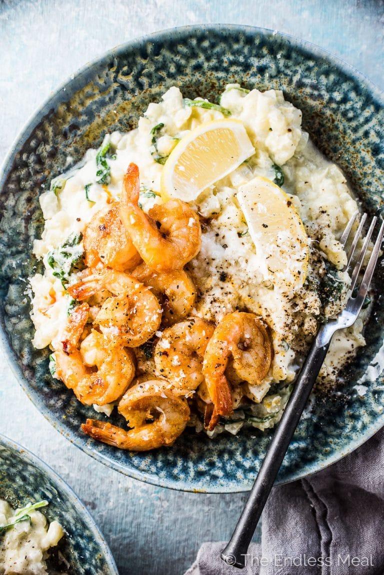 Cauliflower rice risotto and prawns in a blue bowl with a fork.