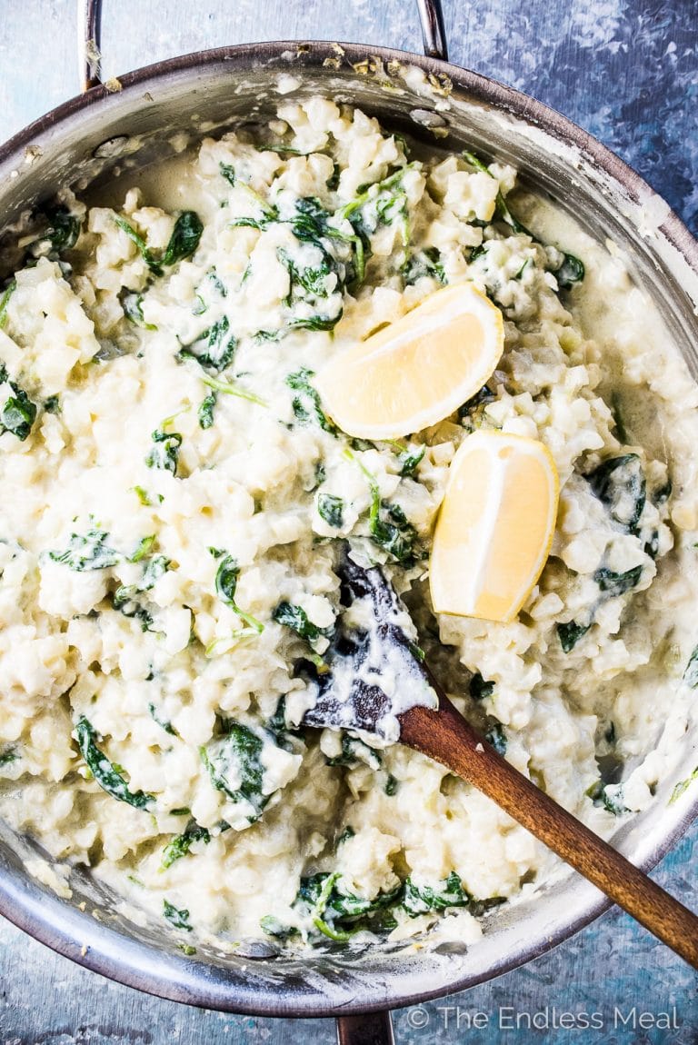 Cauliflower rice risotto on a pan with lemons and spinach.