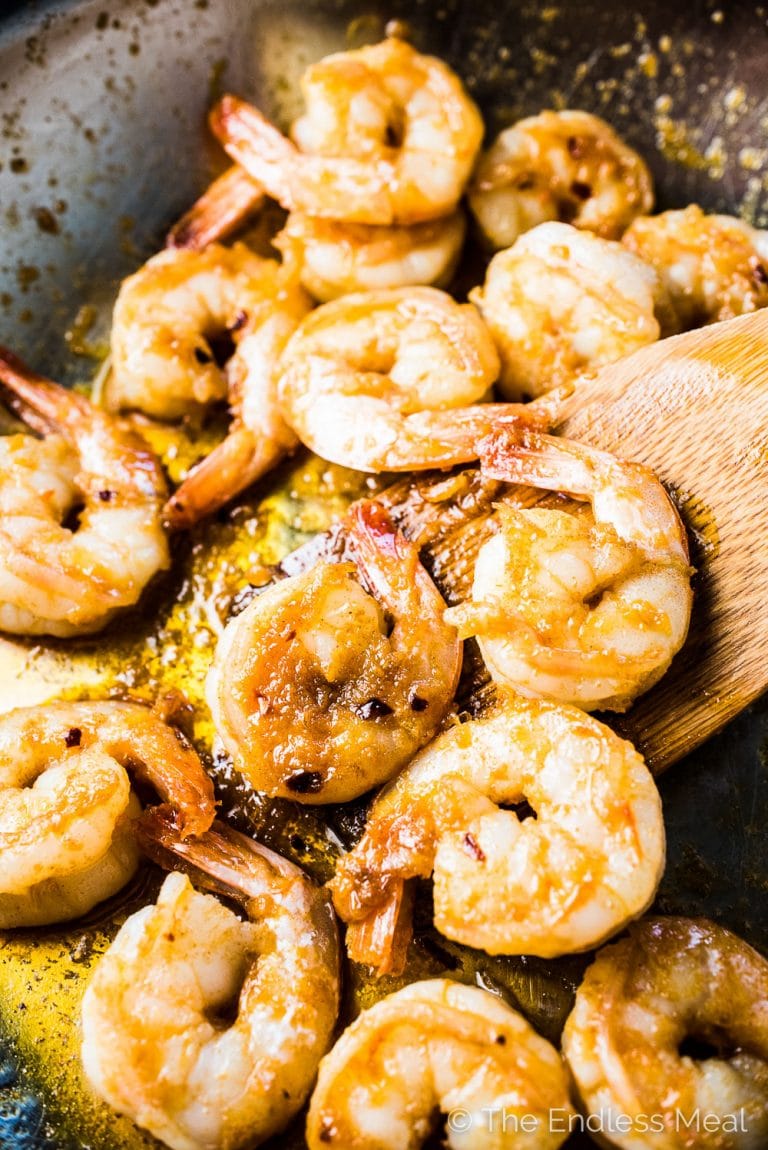 Chili garlic prawns in a pan with a wooden spoon.