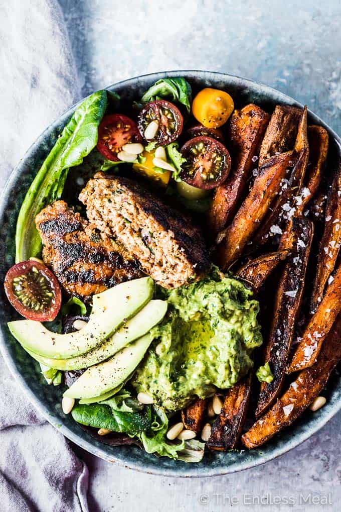 SAVE FOR LATER! Chili Chicken Burger Bowls are everything you love about burgers but served as a bowl. The chicken burger patties are super easy to make and so flavorful. They are grilled or cooked in a pan then served on a bed of lettuce with sweet potato fries and some delicious avocado pesto. You will LOVE them! | gluten-free + paleo + Whole30 | #theendlessmeal #burgers #chicken #whole30 #paleo #glutenfree #chickenburgers #dinnerbowls #bowls
