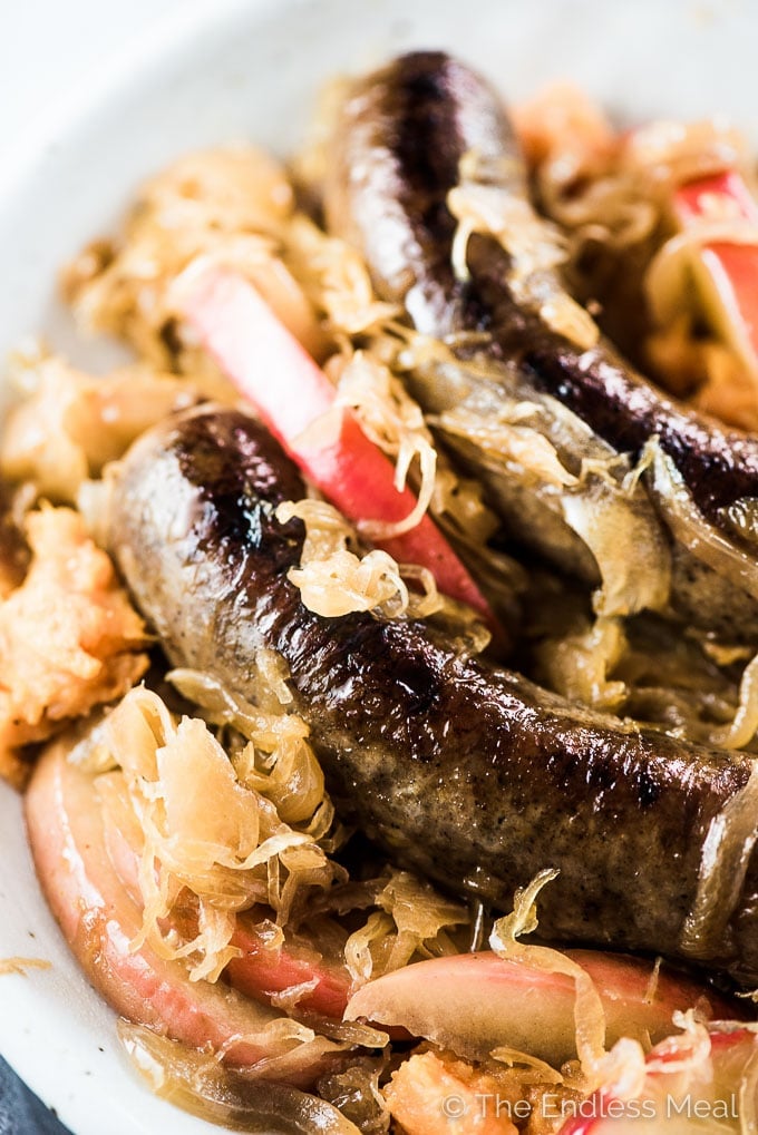 A plate of bratwurst and sauerkraut with slices of red apples.