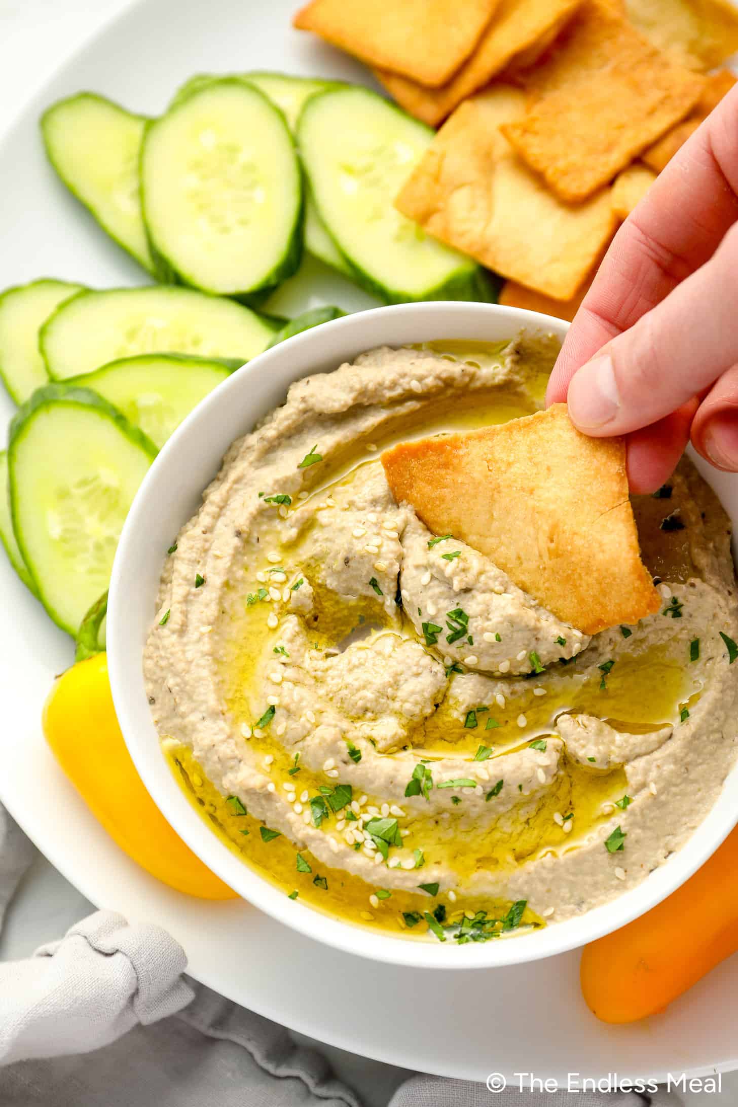 Scooping some Baba Ganoush out of an appetizer bowl with a pita chip