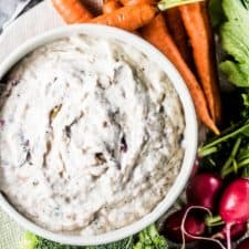 A bowl filled with yogurt and roasted caramelized onion dip with vegetables on the side for dipping.