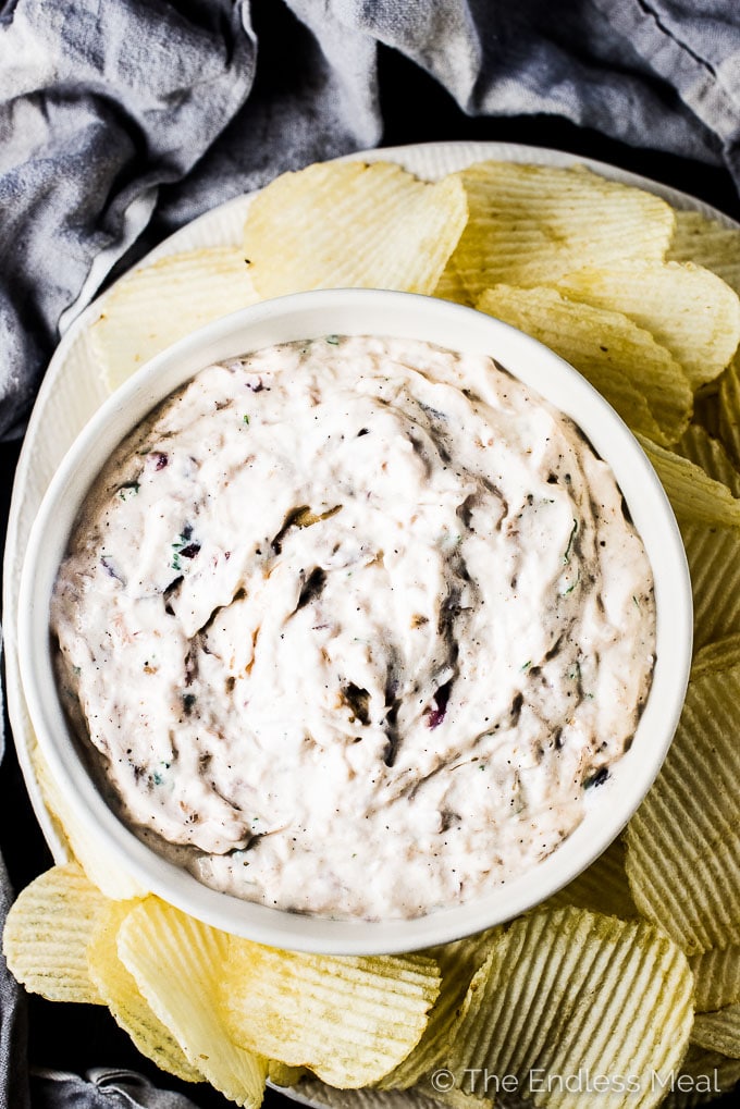 Roasted caramelized onion dip in a bowl with ruffle chips on the side to dip.