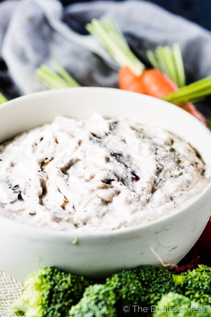 Caramelized onion dip in a white bowl with vegetables on the side for dipping.