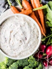 A bowl filled with yogurt and roasted caramelized onion dip with vegetables on the side for dipping.