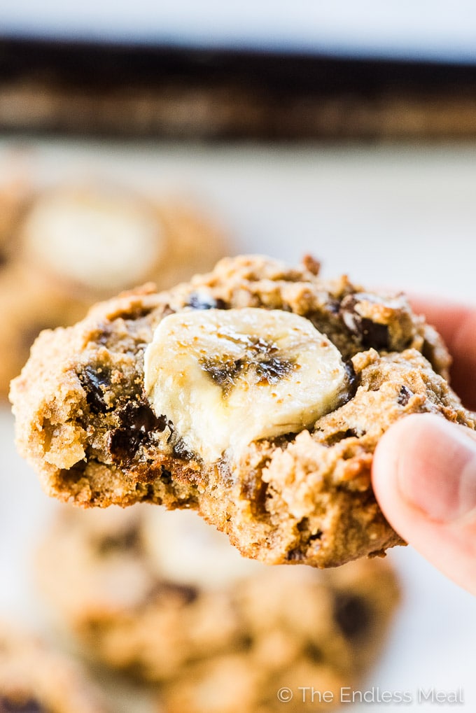 A hand holding chunky monkey paleo banana cookies with a bite taken out of it. 