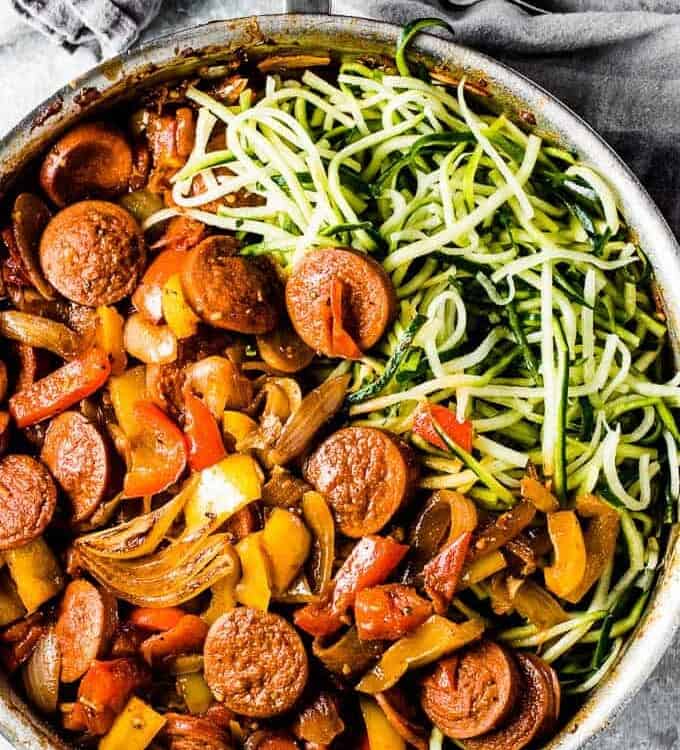 A pan of garlic sausage and peppers with onions on one side and zucchini noodles on the other side.