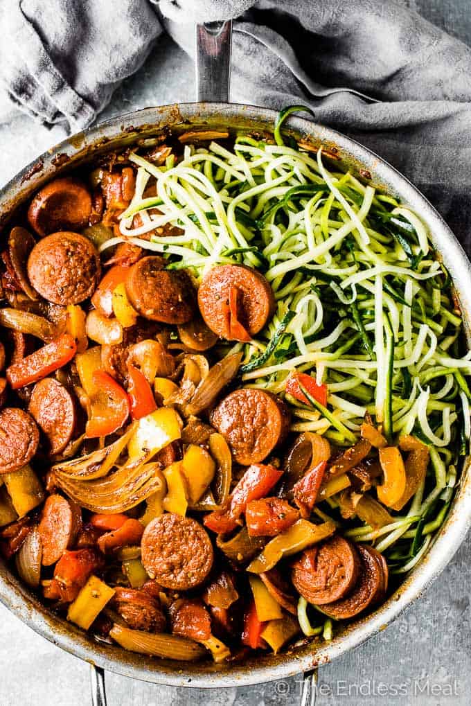 A pan of garlic sausage and peppers with onions on one side and zucchini noodles on the other side.