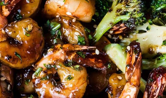 A close up shot of ginger broccoli and sesame honey shrimp in a pan covered with a sticky honey sesame sauce.