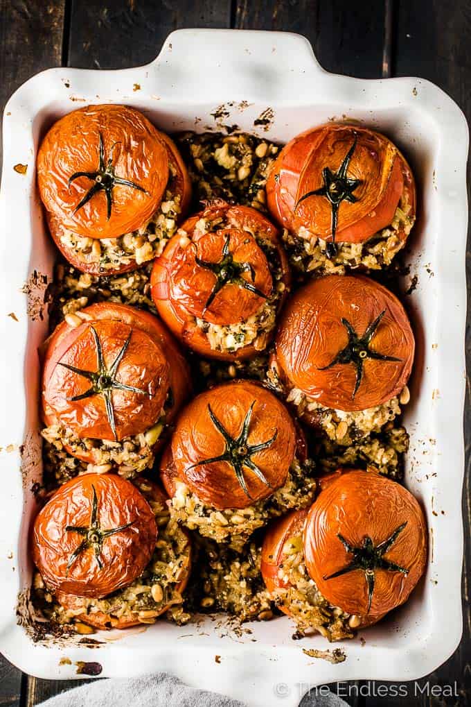 A white baking dish full of tomatoes stuffed with rice hot out of the oven.