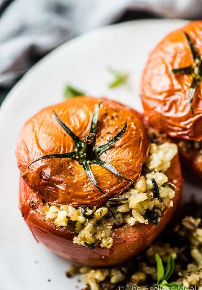 Two tomatoes stuffed with rice on a white plate.