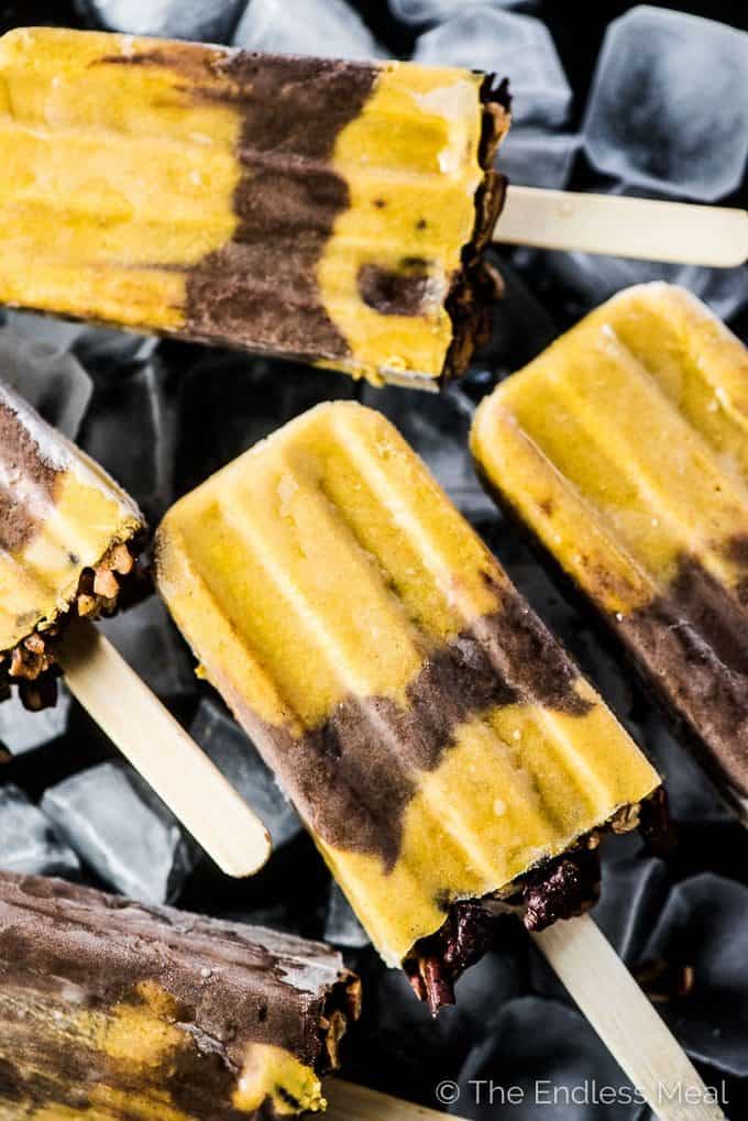 A bunch of pumpkin pie popsicles on a black plate filled with ice.