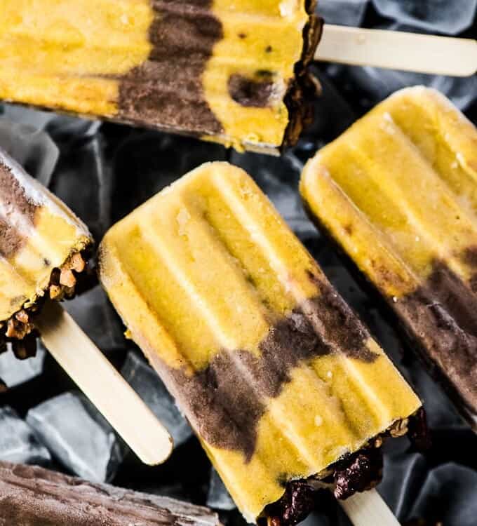 A bunch of pumpkin pie popsicles on a black plate filled with ice.